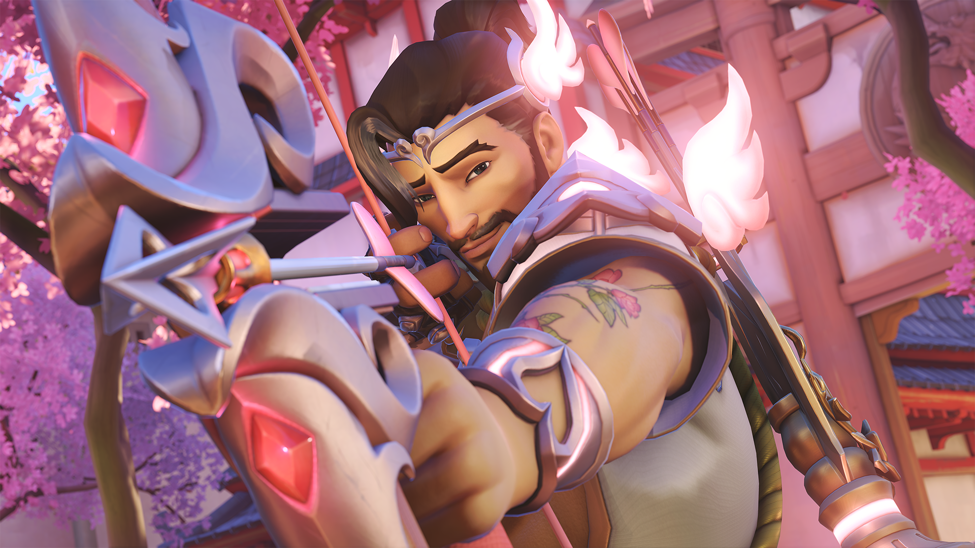 Cupid Hanzo pulling back an arrow in his bow, which has red gems on it. He’s got a flower tattoo on his arm, and his shoulders and thin silver headpiece have pink cloud-like wings on them. In the background is a cherry blossom tree.